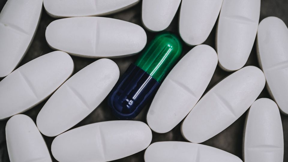 A green and blue pill capsule surrounded by white tablets.