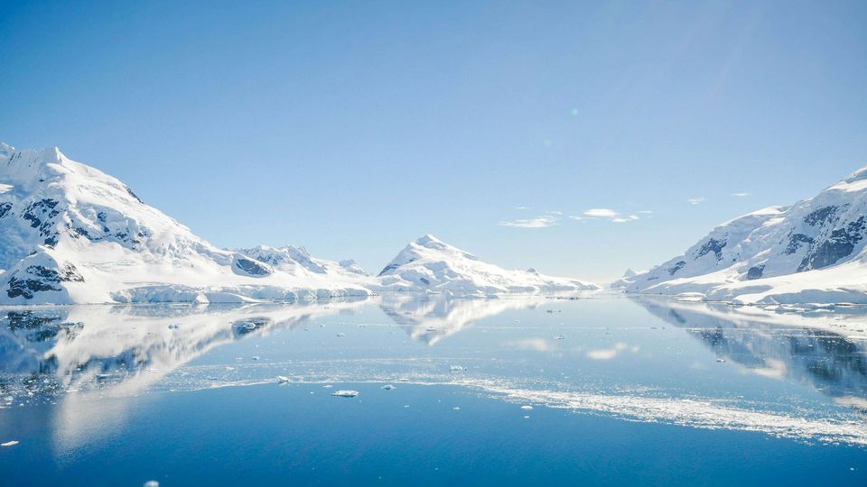 Snowy mountains with dark rock visible underneath next to the sea.