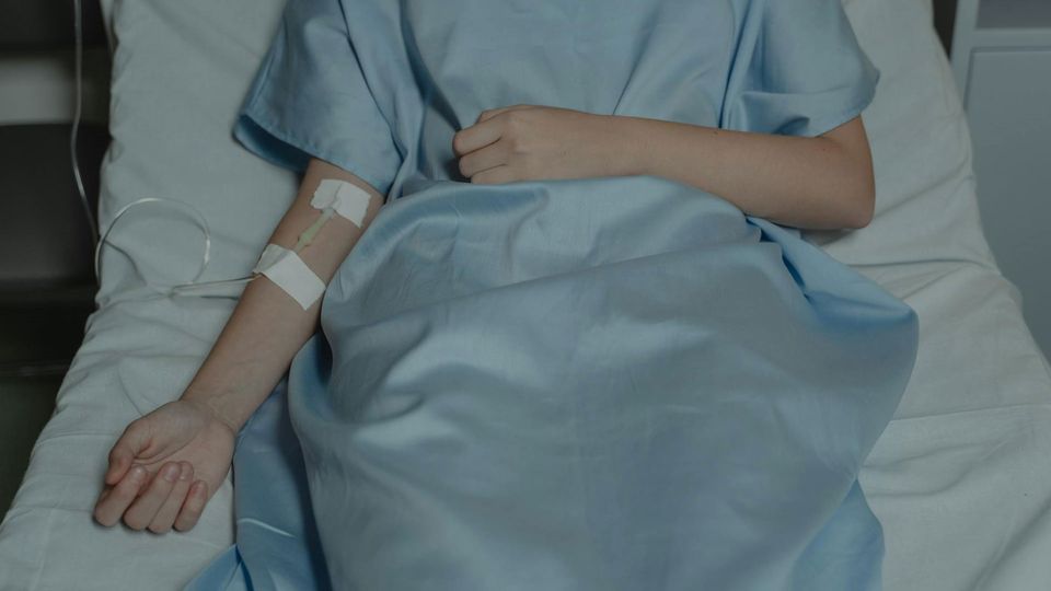 A cancer patient in a hospital bed with a drip attached to their arm.