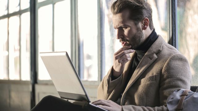A man looking at a laptop screen with his hand on his chin in deep thought.