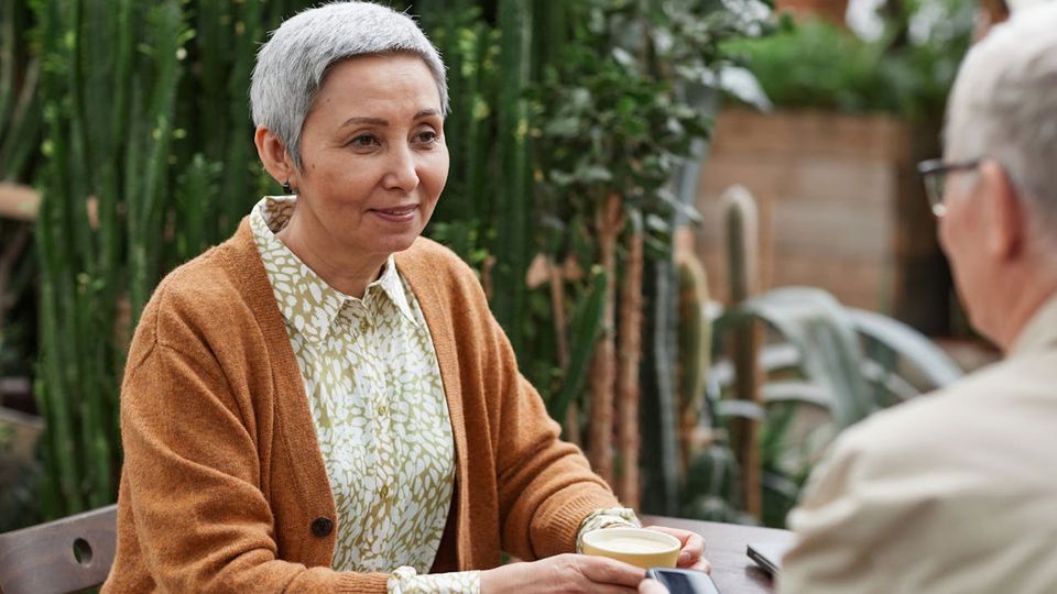 A woman with grey hair holds a cup of coffee.