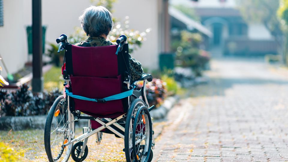 An elderly woman sitting in a wheelchair looking out at the distance.