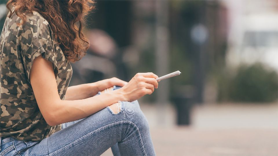 A woman sits outside with an unlit marijuana joint, a source of THC.