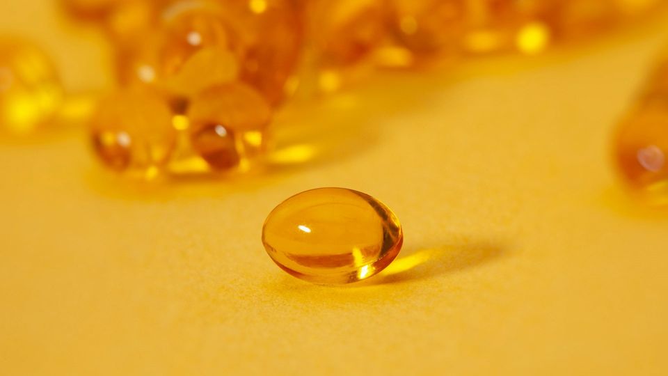 A golden vitamin D capsule on a yellow background.