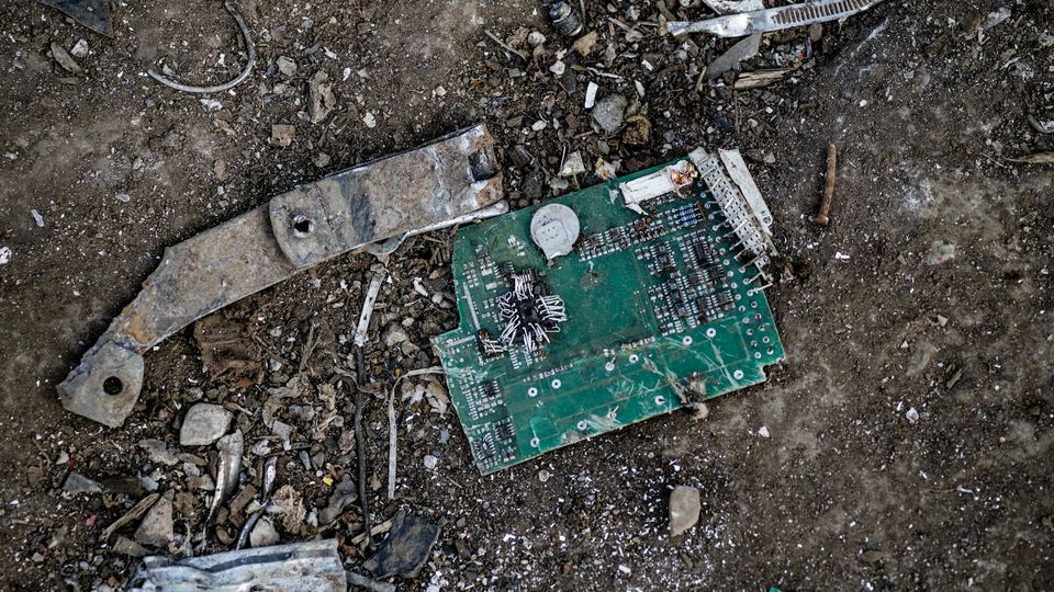 A discarded circuit board lies in the dirt.