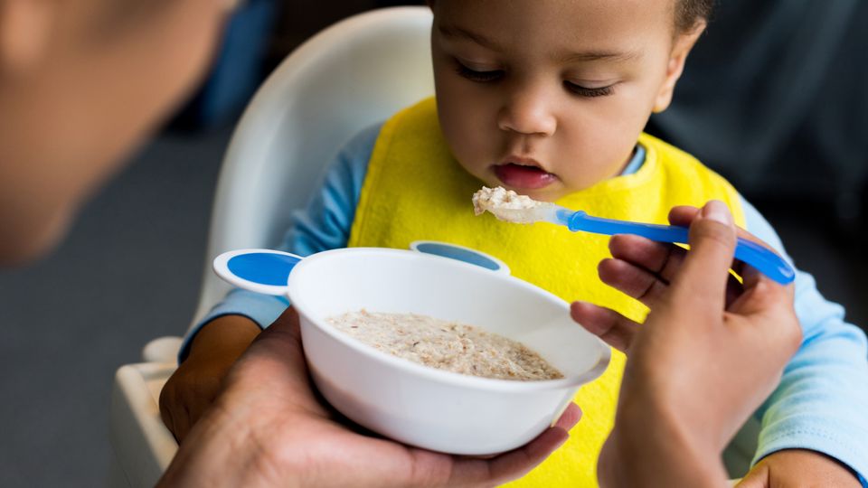 A baby/toddler is fed a spoonful of porridge/cereal