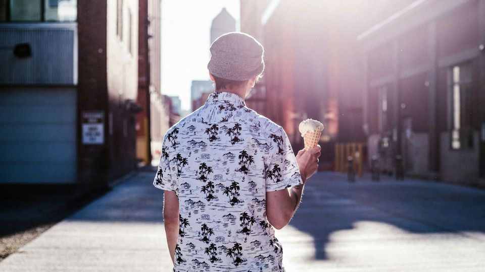 A person in a city, wearing a patterned shirt and holding an ice cream
