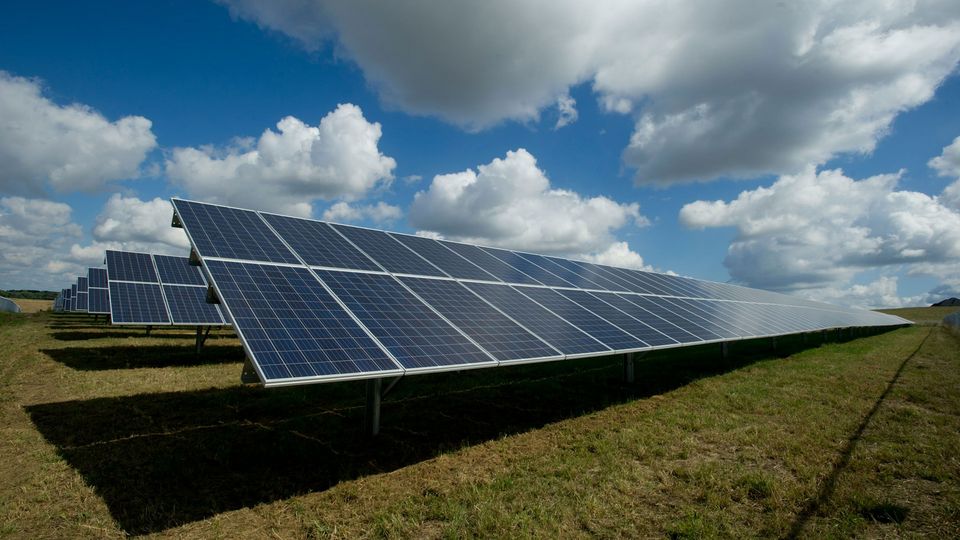 Solar panels in a field, under a blue sky with white clouds.