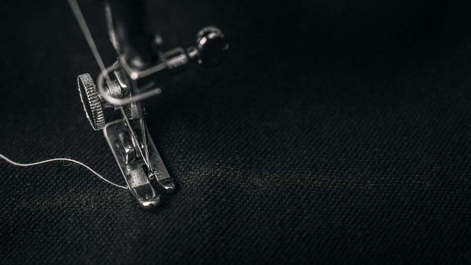 A black and white image of a sewing machine foot preparing to sew white thread into black fabric.