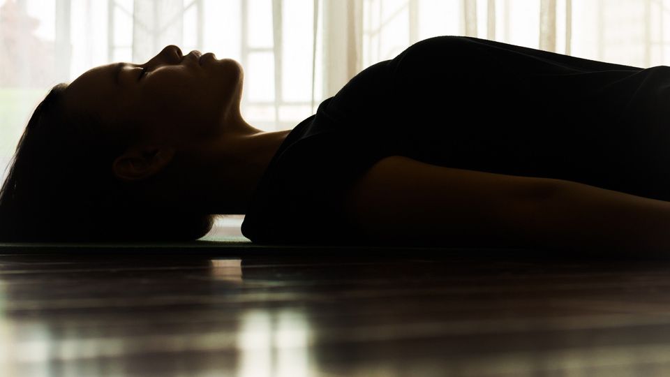 A woman lying down on the ground with her eyes shut.