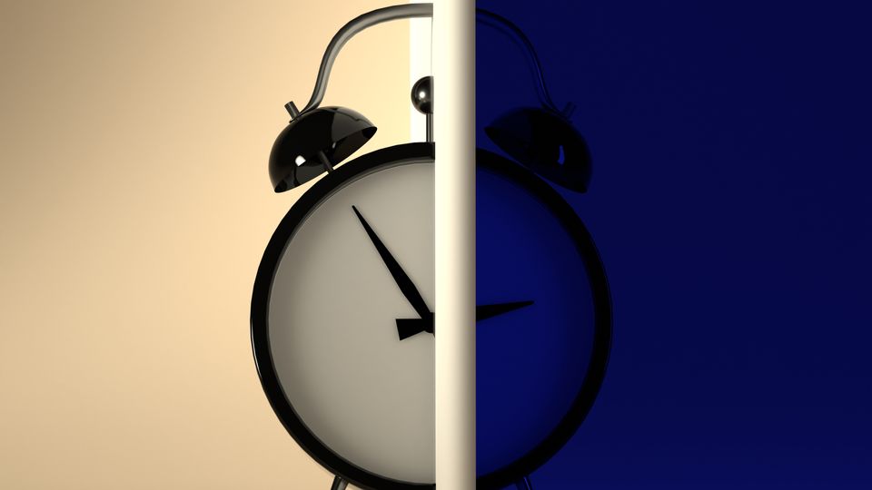 An alarm clock, half in the light, half in the dark.