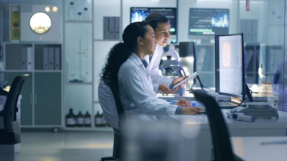 Two scientists in lab coats at a computer in a lab.