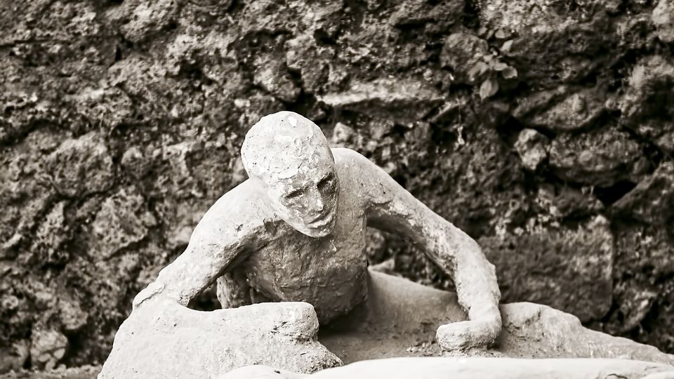 Plaster cast of a victim of the Mount Vesuvius eruption in Pompeii, preserved in detail against a stone backdrop.
