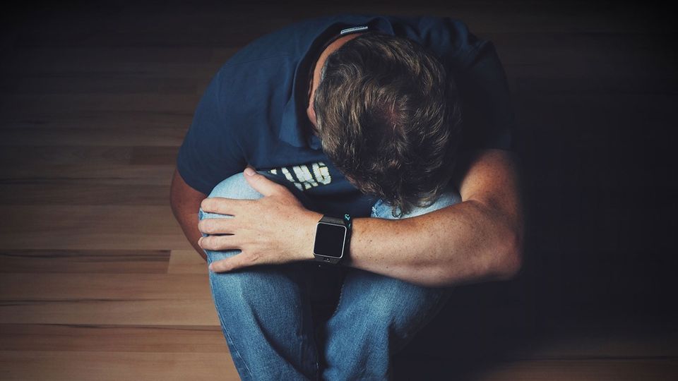 Man sitting on fall in a ball with head on knee.