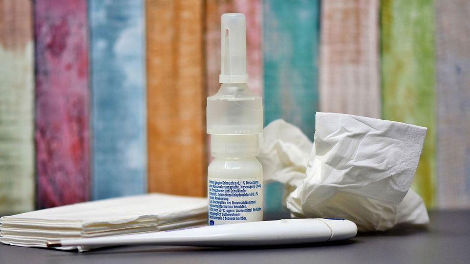 A close-up of a nasal spray bottle, accompanied by tissues and a thermometer, arranged on a table.