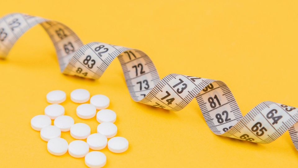 A curling tape measure next to white pills on a yellow background.