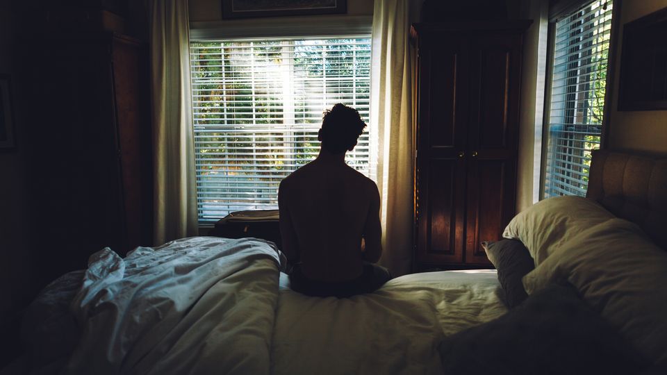 A person sitting on a bed in a dark room.