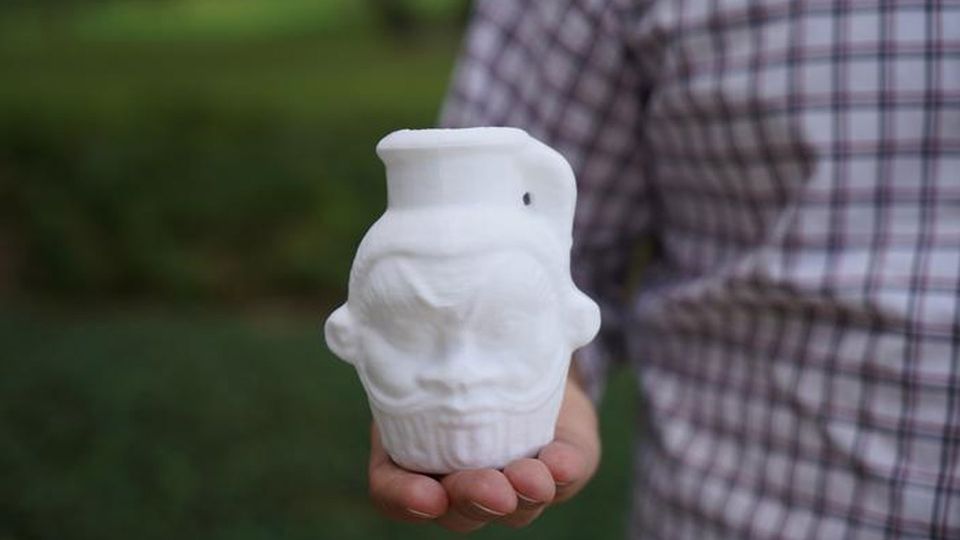 A man holds a white 3D replica of an Egyptian Bes mug.
