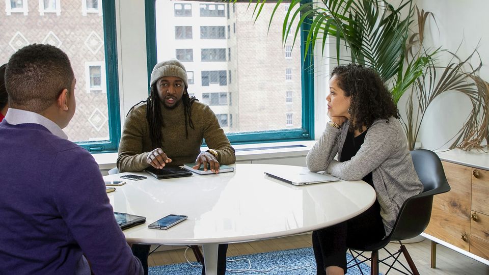 A group of people sat around a white office table, discussing ideas.