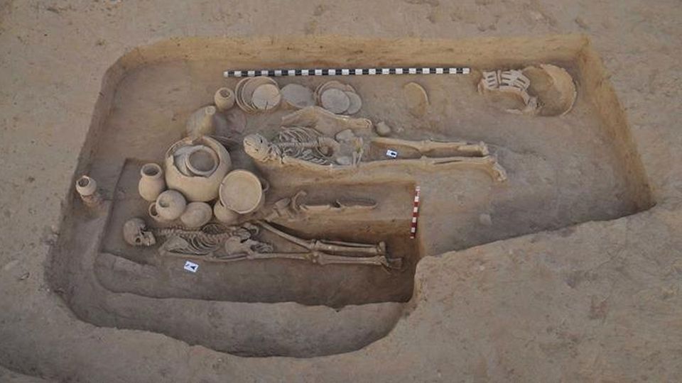 A pair of human skeletons in an excavation site, with pottery bowls and urns around them.