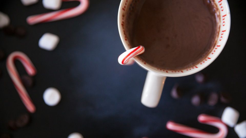 A mug of hot chocolate with a candy cane in it.