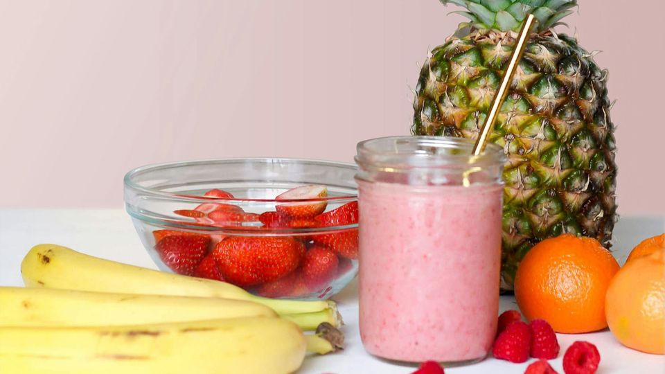 A pink smoothie surrounded by fruits.