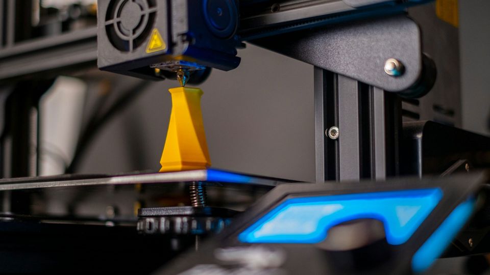 A 3D printer creates a twisted column out of yellow material.