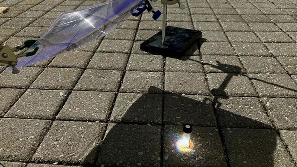 A curved plastic screen directs sunlight at a clear vial, where black plastics are recycled.