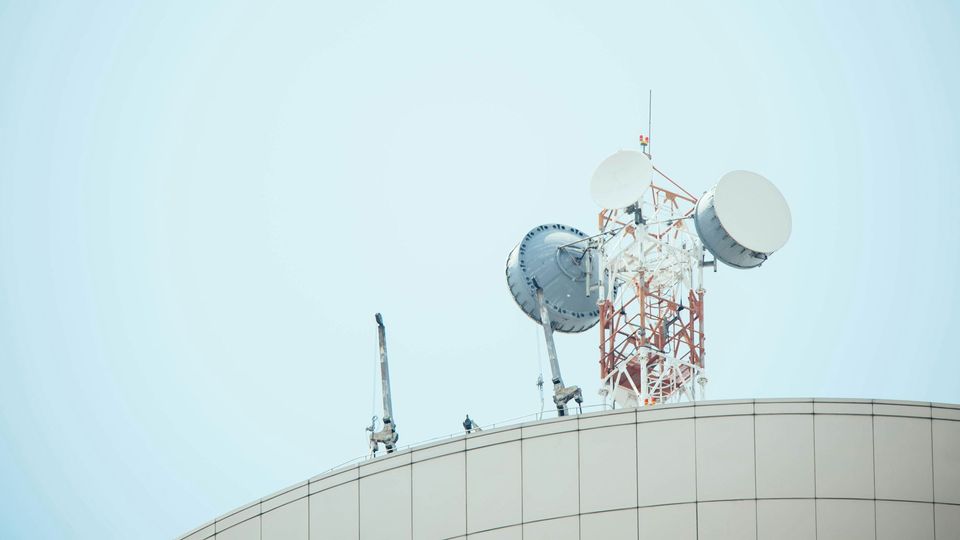 A white antenna pole with three antennae on it against a pale blue sky.