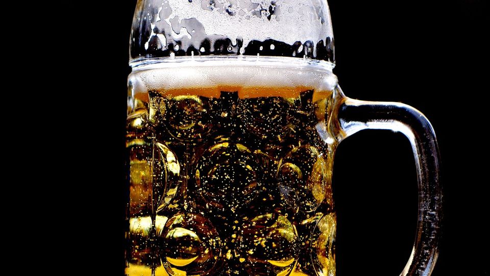 Beer stein filled with golden beer and bubbles against a dark background.
