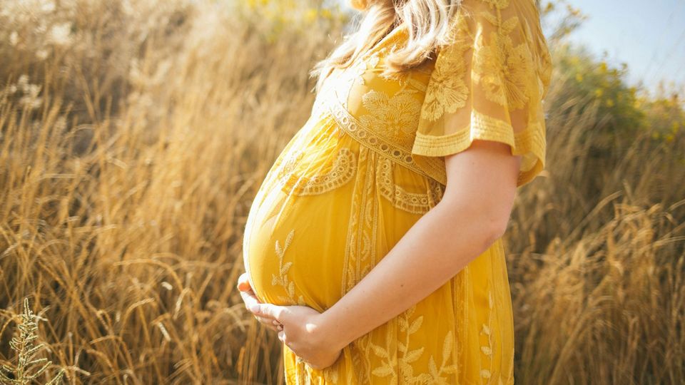 A pregnant woman in a yellow dress holds her bump.