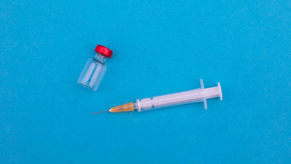 A drug vial and a syringe on a blue background.