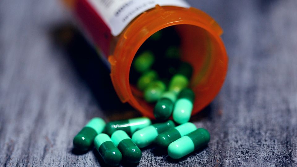 Teal and green pills spill from a prescription bottle.