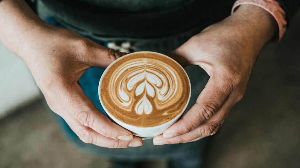 A person holds a cup of coffee with latte art on the top.