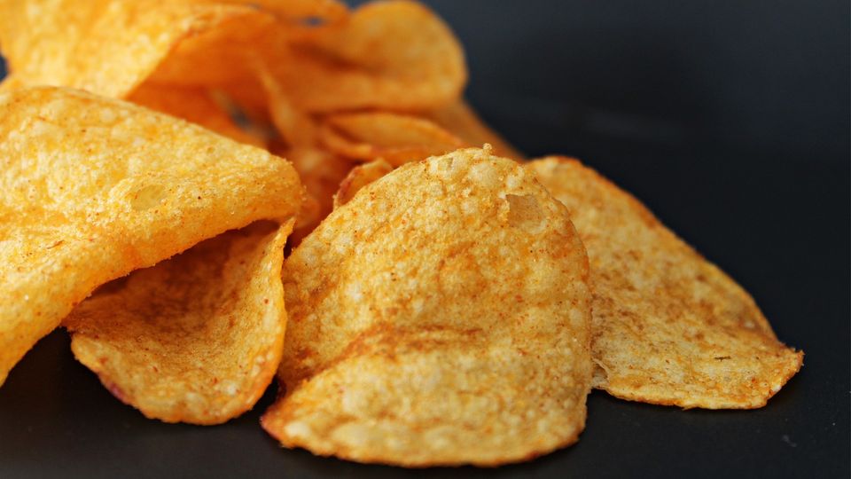 A pile of spicy potato chips, lying on a dark surface.