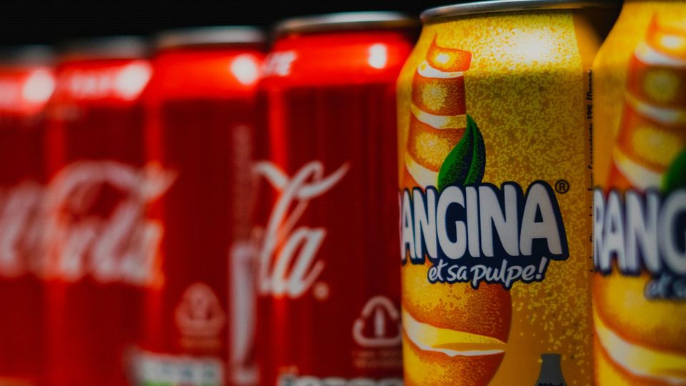 Red and yellow cans of soda lined up on a shelf.