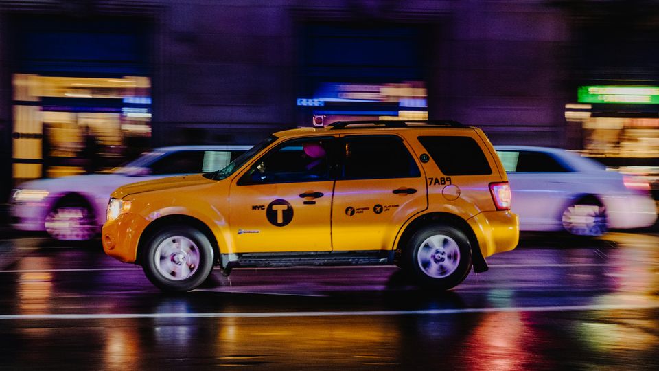 A yellow New York City taxi in motion on a rainy street at night, with blurred lights in the background.
