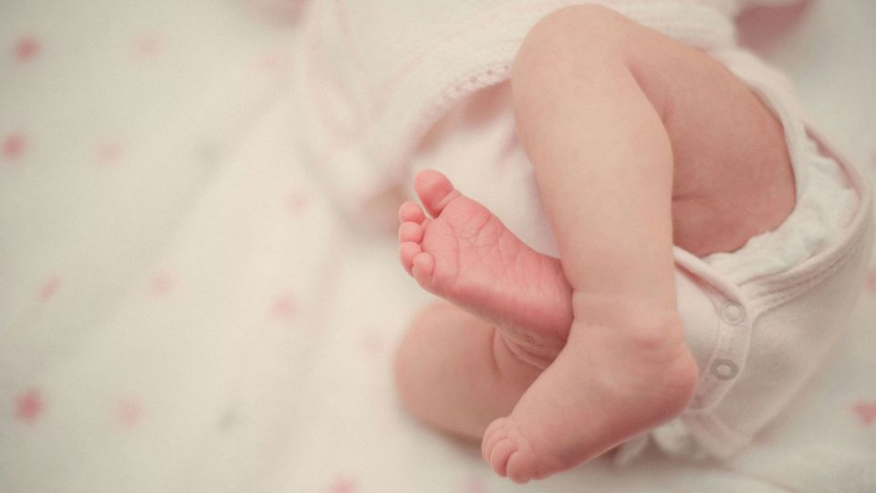 A baby's legs and feet, with a diaper slightly visible underneath a romper.