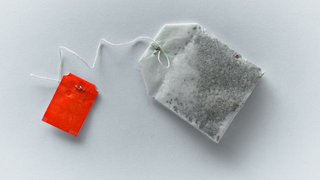 A tea bag with a red label on a white desk, a potential source of microplastics and nanoplastics. 