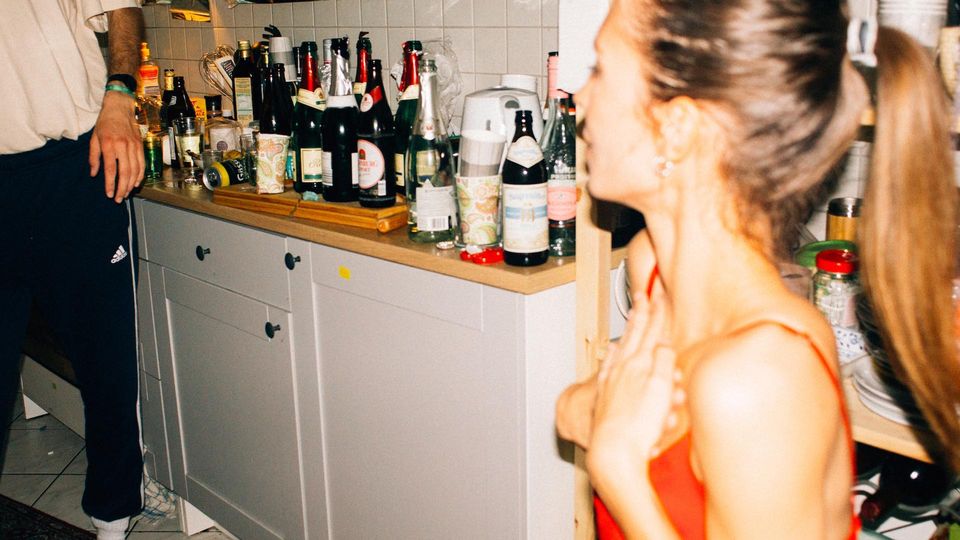 Woman at a party near a countertop filled with alcohol bottles, illustrating the concept of female binge drinking.