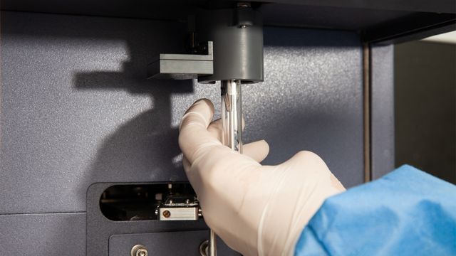 Gloved hand placing a sample tube into a flow cytometry machine for cell analysis. 