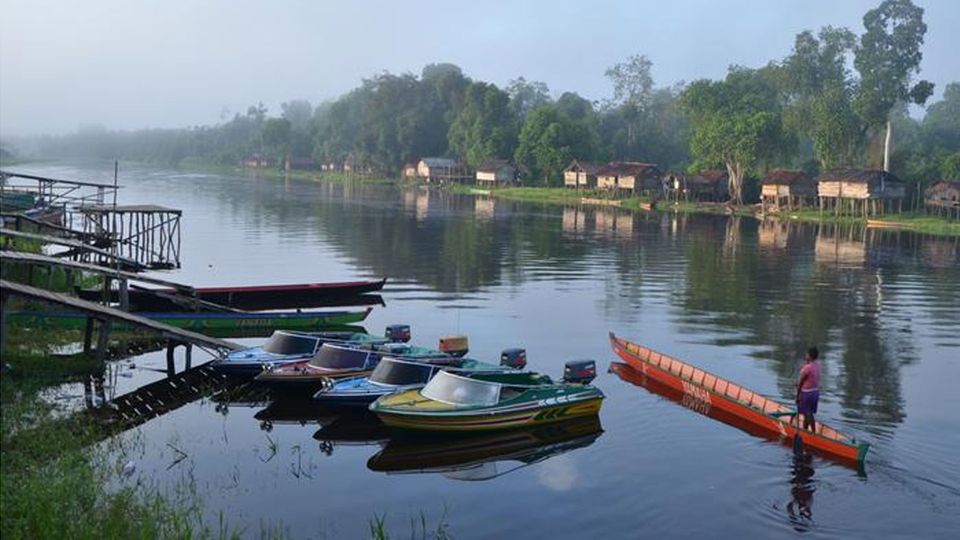A few small electric boats and a person in a canoe on a river near a small settlement.