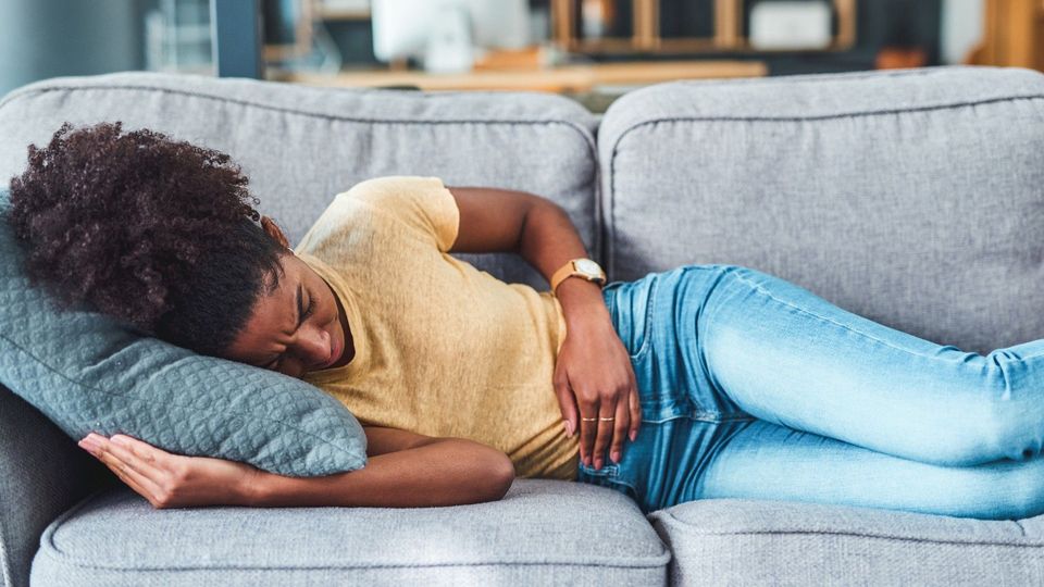 A young woman led on a sofa suffering from stomach pain. Highlighting the need for gut organoids to study IBD.