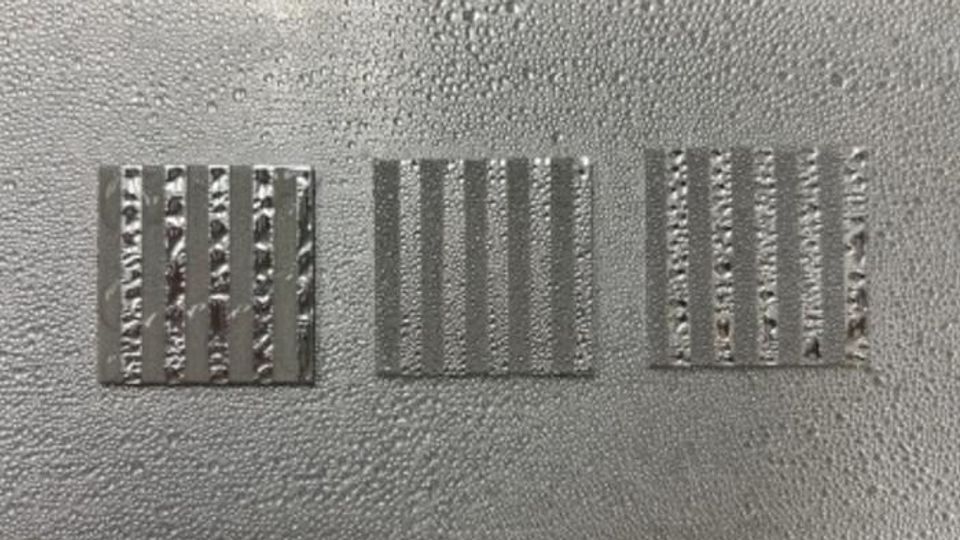 Aluminum coupon samples patterned with alternating stripes of smooth (lighter) and etched (darker) topographies display contrasting wettability.