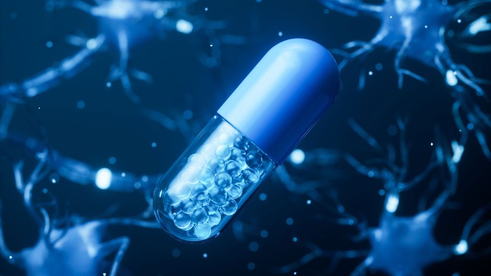 A drug capsule filled with small beads, with cells in the background.