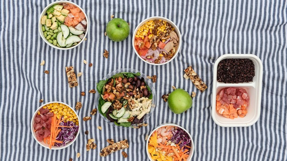 Bowls of different salads on a picnic rug.