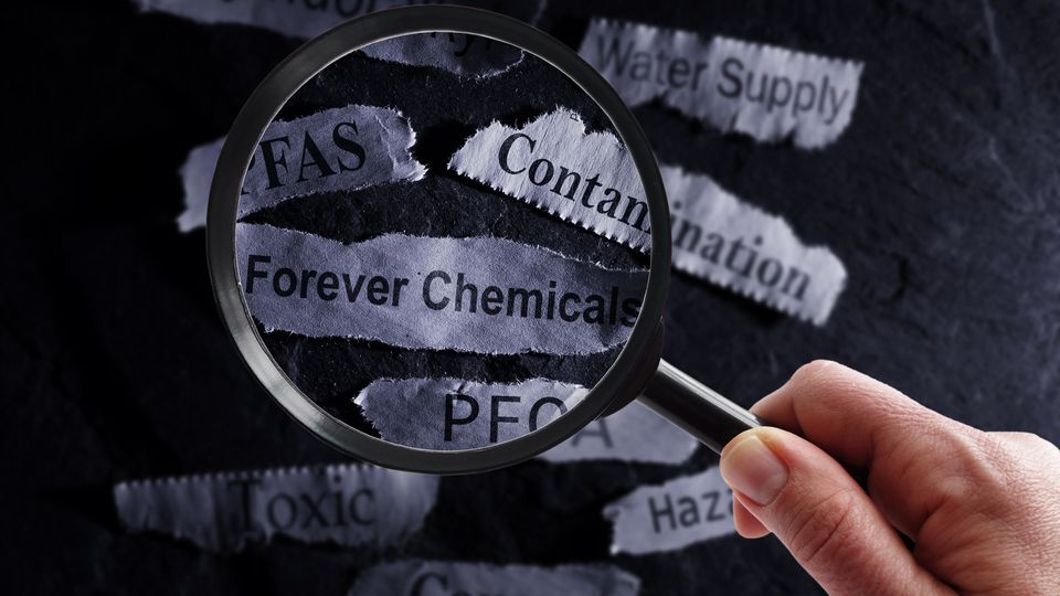 A magnifying glass held over pieces of paper that read words related to PFAS.
