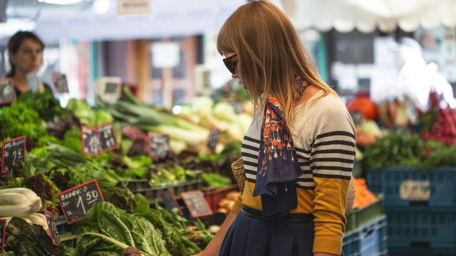 A woman looks at fresh vegetables on a market stall.