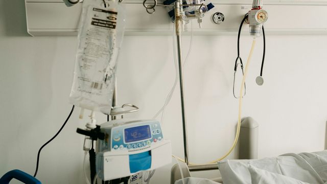 A hospital bed with a drug drip stand, a monitor and a stethoscope.