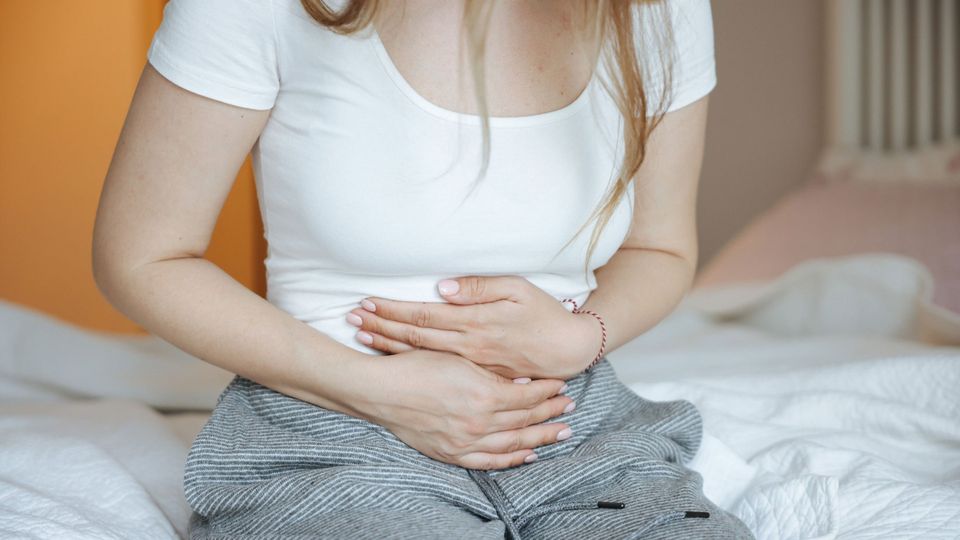 A woman in a white t-shirt holds her stomach.